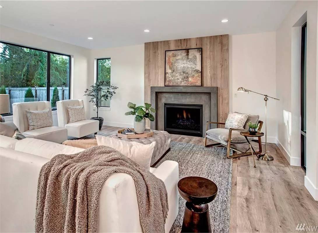 Great room with beige seats, a tufted ottoman, and a fireplace against a wooden accent panel.