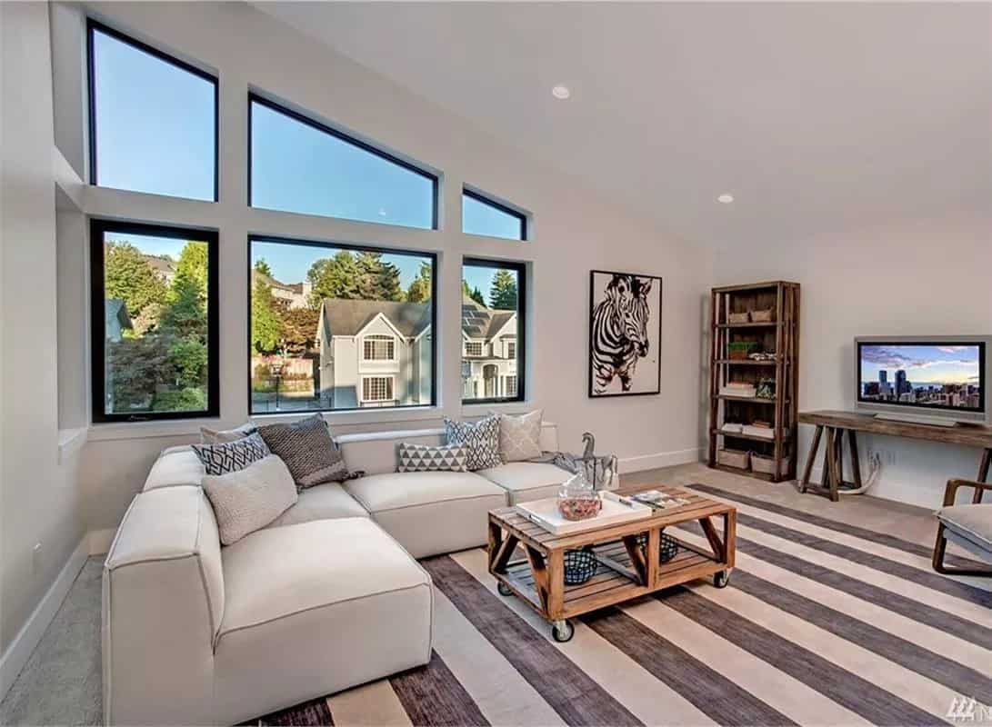 Bonus room with an L-shaped sectional and wooden tables under a shed ceiling.