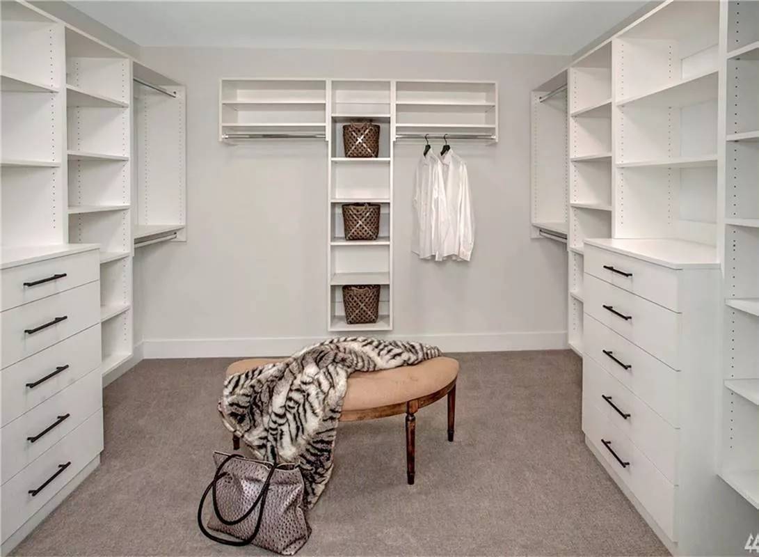 Primary walk-in closet with white built-ins and a curved bench over the carpeted floor.