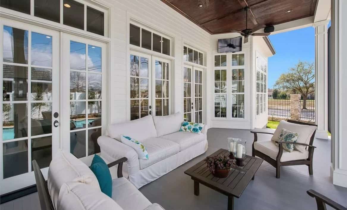 Covered porch with skirted sofas, cushioned chairs, and a matching coffee table under a wood-paneled ceiling.