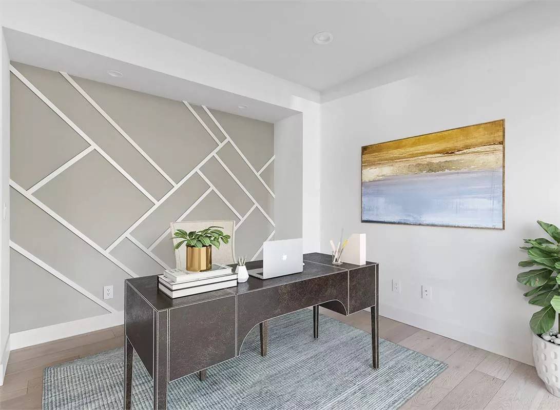 Home office with a geometric accent wall and a dark wood desk over a gray area rug.