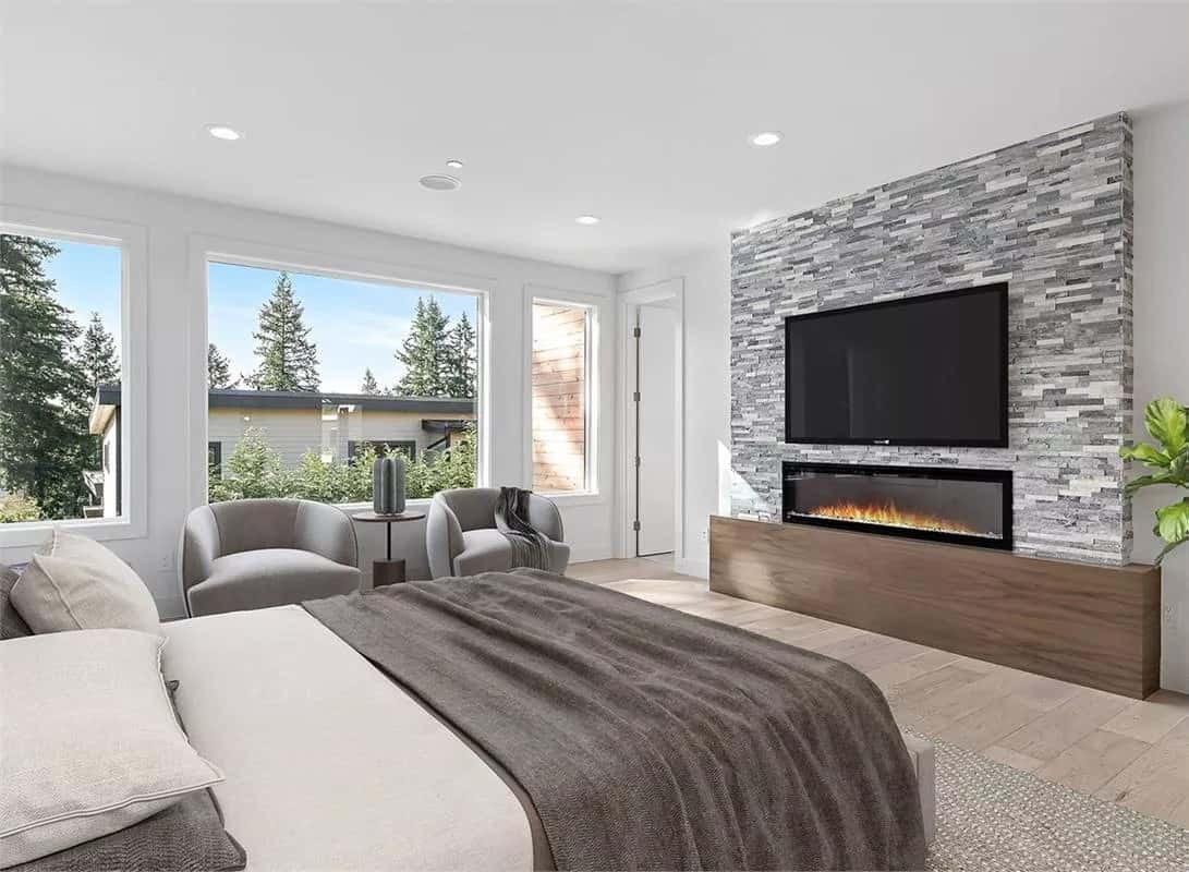 Primary bedroom with round back chairs and a stone fireplace topped with a TV.
