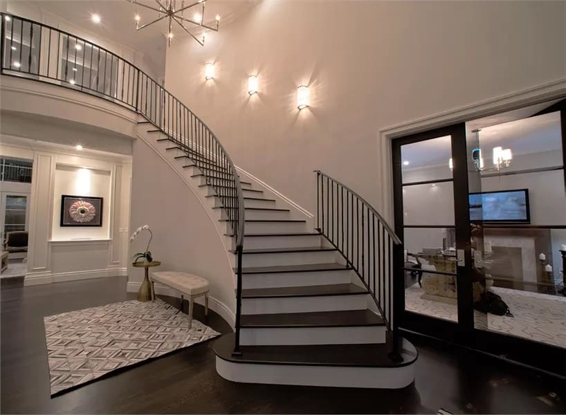 Foyer with a curved staircase and a French door that reveals the quiet den.