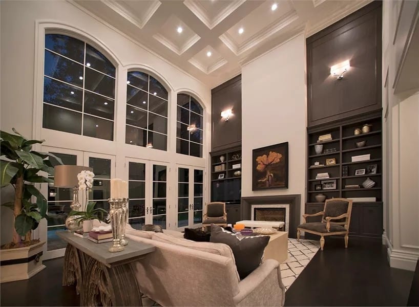 Great room with huge windows, a coffered ceiling, and an electric fireplace flanked by dark wood built-ins.