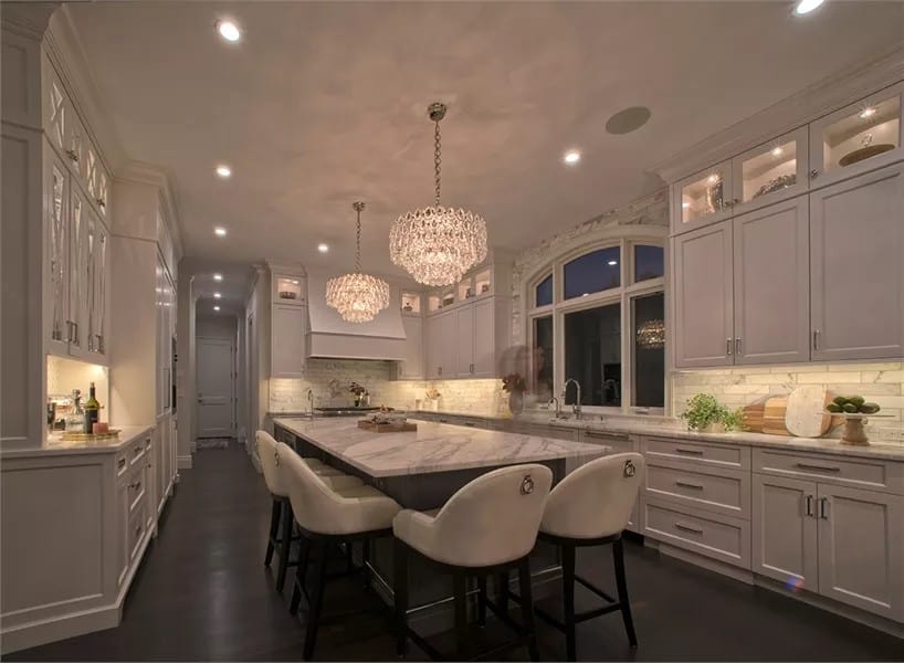 Kitchen with white cabinetry, marble countertops, and a center island surrounded by modern bar stools.