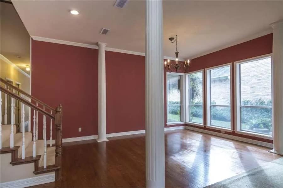 Dining room with red walls and huge windows that look out the lush yard.