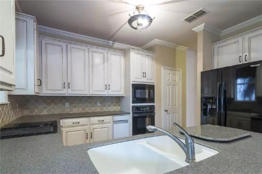 The kitchen includes black appliances and double sinks fitted on the peninsula bar.
