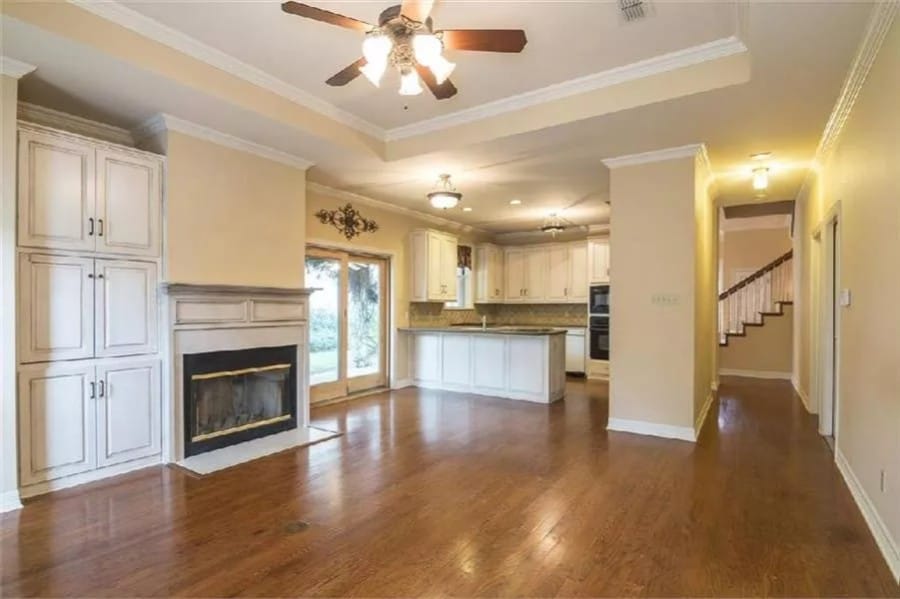 Family room with a glass-enclosed fireplace and a tray ceiling mounted with a fan.