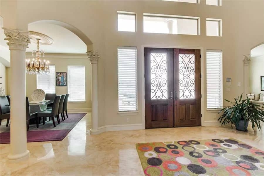 Foyer with a French front door and a patterned area rug that lays on the marble tiled floor.