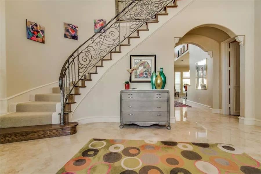 The foyer includes a wooden dresser and an intricate curved staircase leading to the secondary bedrooms.