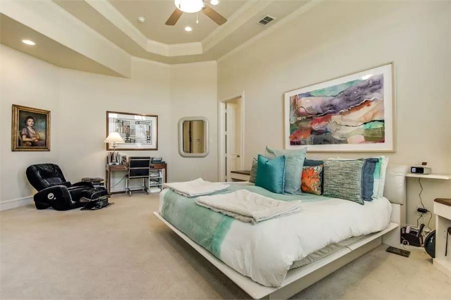 Primary bedroom with a platform bed, a wooden desk, and a leather lounge chair under a high tray ceiling.