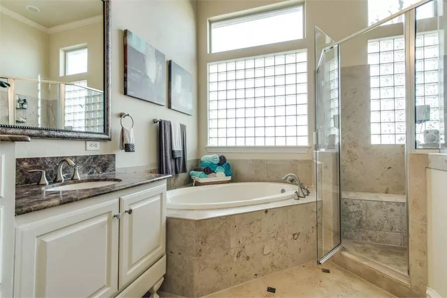 Primary bathroom with a sink vanity, a corner tub, and a walk-in shower with a tiled bench.