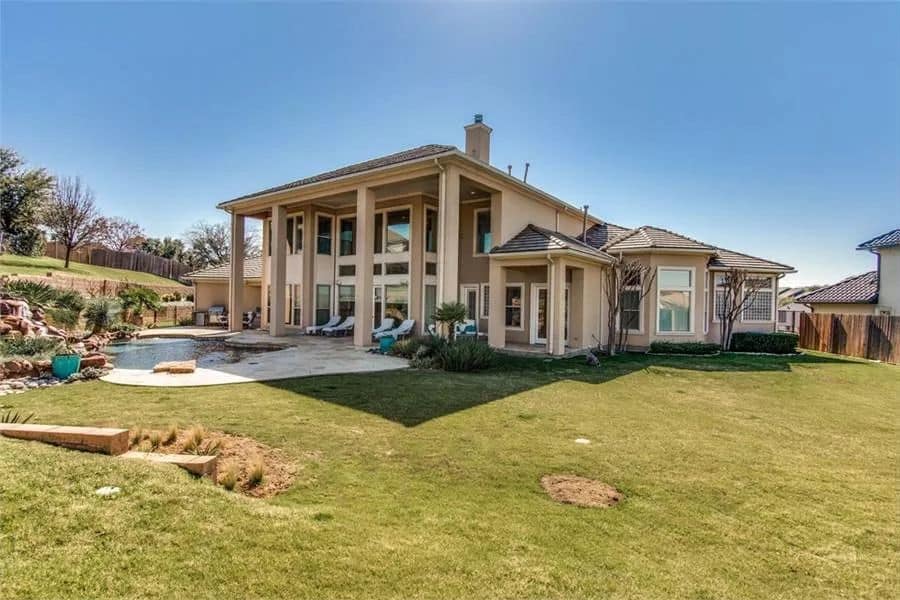 Rear view of the house with huge windows and a covered veranda framed with towering pillars.