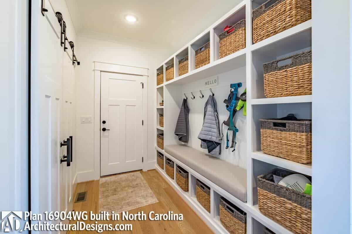 Utility room with a cushioned bench, coat hooks, and built-in cubbies filled with rattan baskets.
