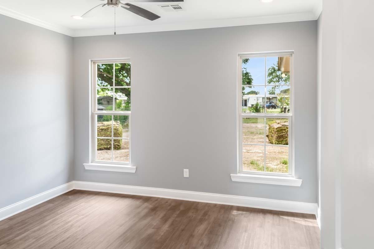 Primary bedroom with a hardwood floor, gray walls, and white-framed windows looking out the backyard.