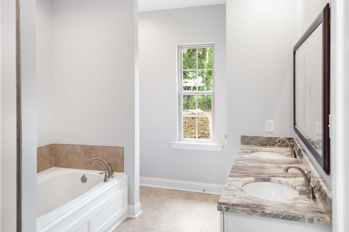 Primary bathroom with a bathtub and a dual sink vanity topped with a rectangular mirror.