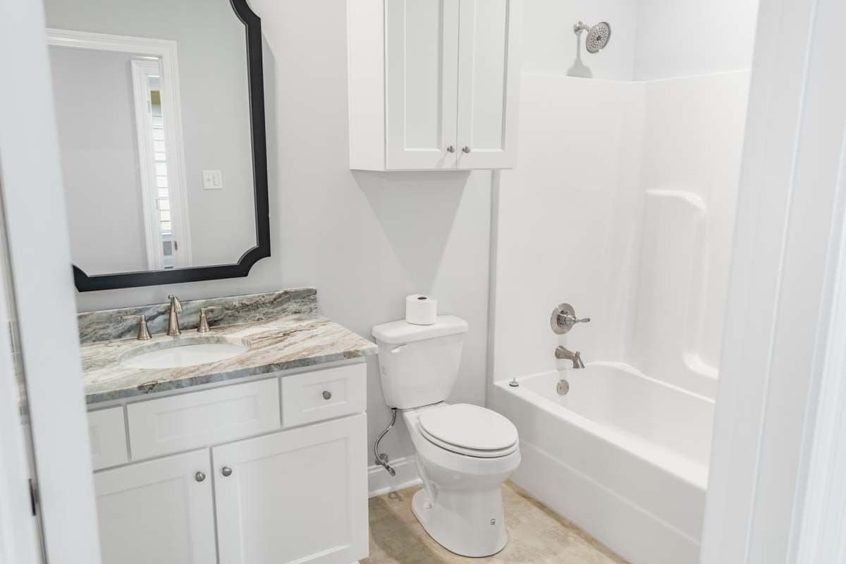 Bathroom with a sink vanity, a tub, and shower combo, and a toilet topped with an overhead cabinet.