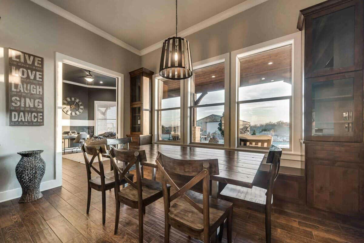 Dining room with gray walls, a rustic dining set, and a trio of windows overlooking the covered patio.