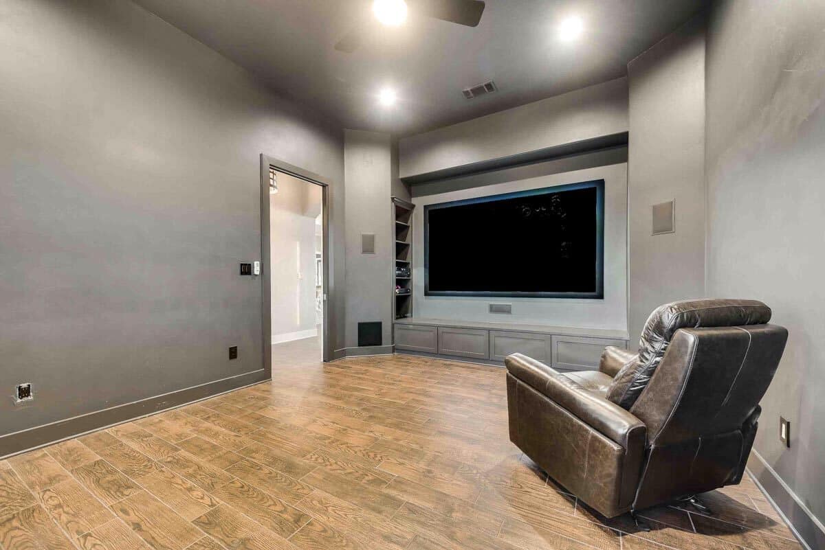 Media room with a large TV and a leather recliner over the wide plank flooring.