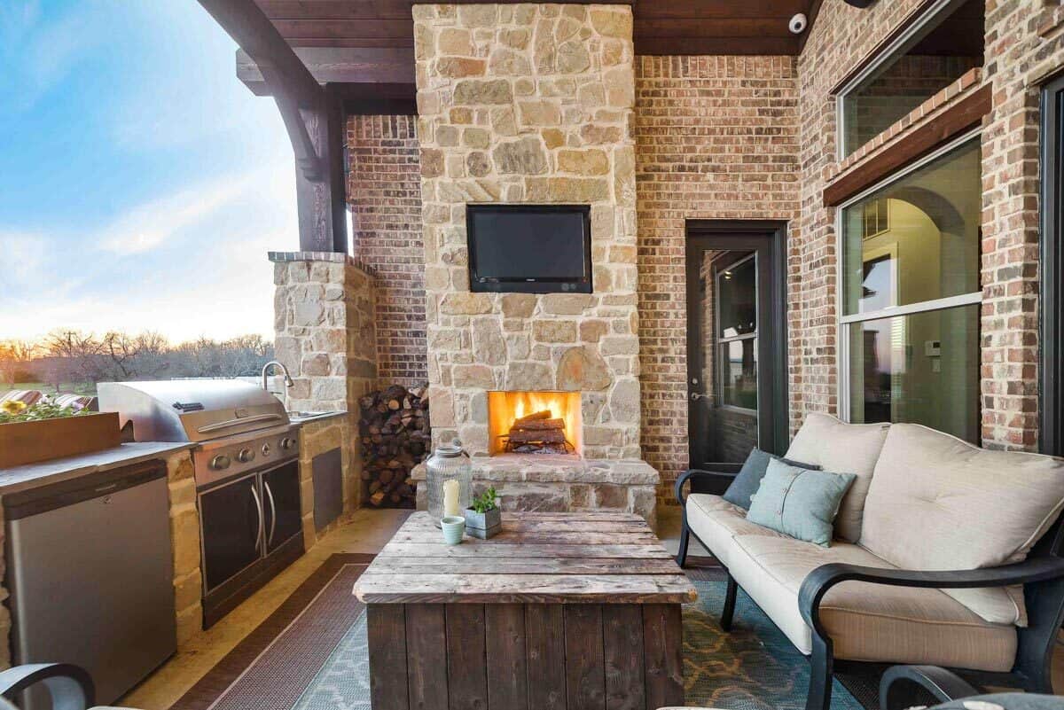 Outdoor living with a stone fireplace, a summer kitchen, and a cushioned sofa paired with a rustic coffee table.