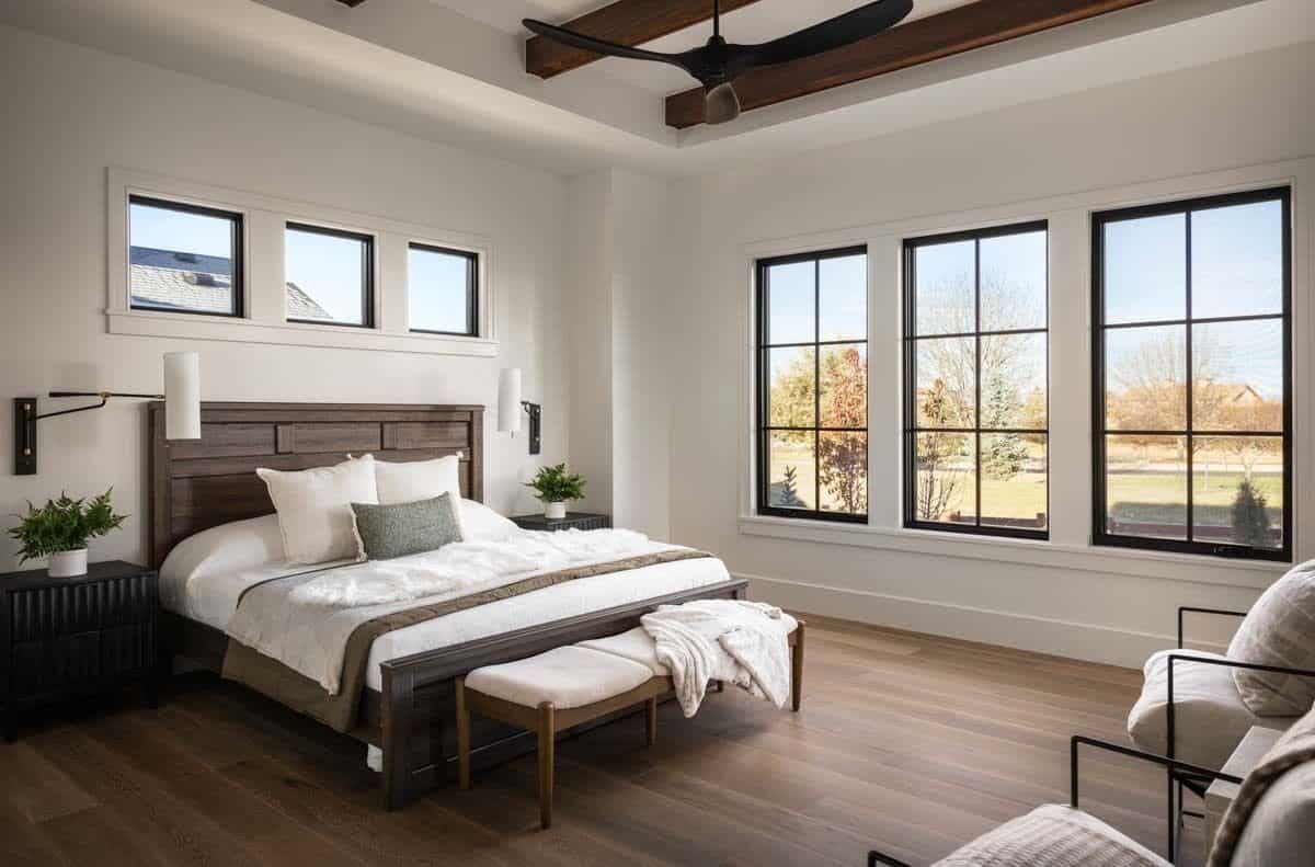Primary bedroom with a dark wood bed, matching footstools, and metal chairs under the tray ceiling with exposed beams.