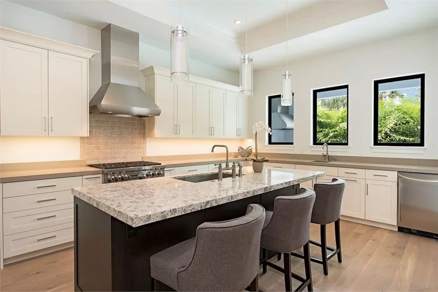 Kitchen with white cabinetry, a trio of windows, and a breakfast island under a tray ceiling.