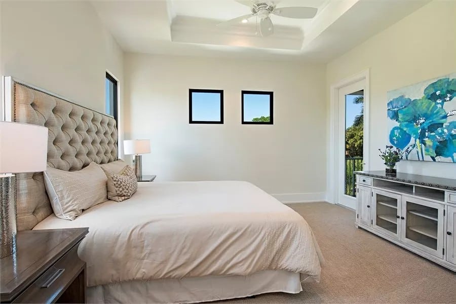 Bedroom with a leather tufted bed and a wooden dresser adorned by a floral painting.