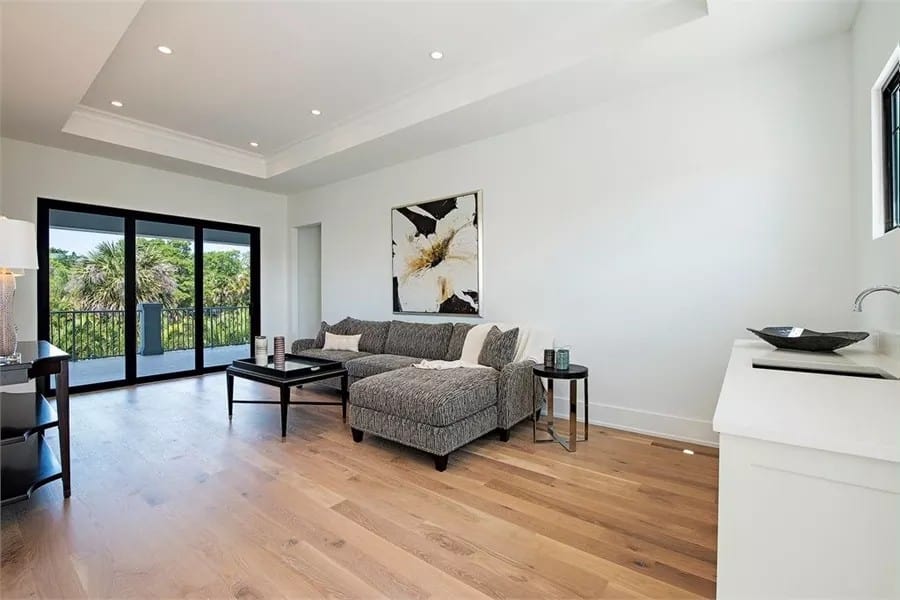 Lounge area with a tray ceiling, an L-shaped sofa, a wet bar, and balcony access through sliding glass doors.