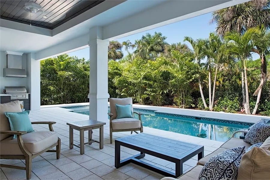 Covered lanai with cushioned seats, wooden tables, and an attached swimming pool.