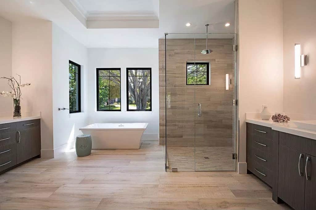 Primary bathroom with a walk-in shower, his and her vanities, and a soaking tub under the picture windows.