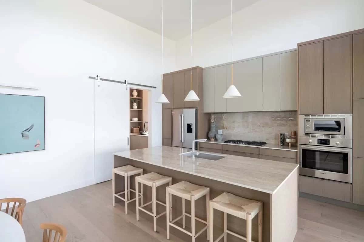 Kitchen with light wood cabinets ad a matching center island lined with four bar stools.