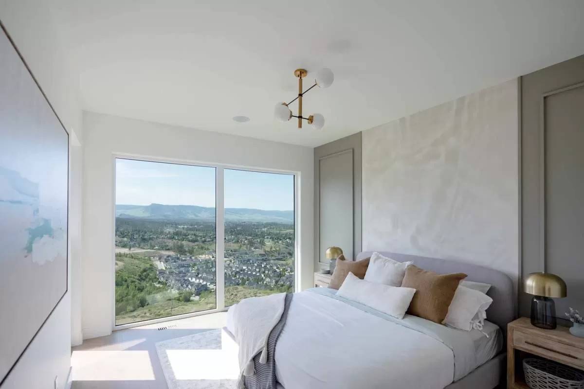 Primary bedroom with a carpeted floor and huge windows overlooking the surrounding landscape.