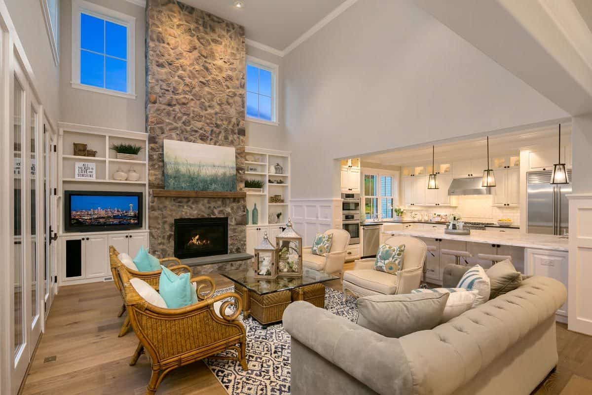 Family room with a tufted sofa, wicker chairs, and a stone fireplace under a tall ceiling.