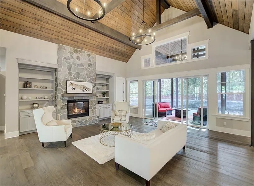 Great room with beige seats, a round coffee table, and a stone fireplace flanked by white built-ins.