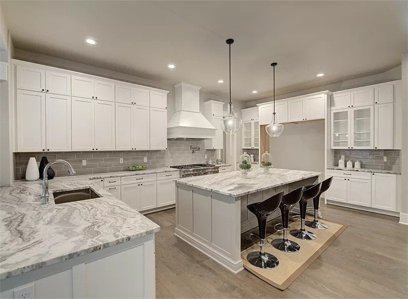 Kitchen with white cabinetry, marble countertops, and a center island paired with modern bar stools.