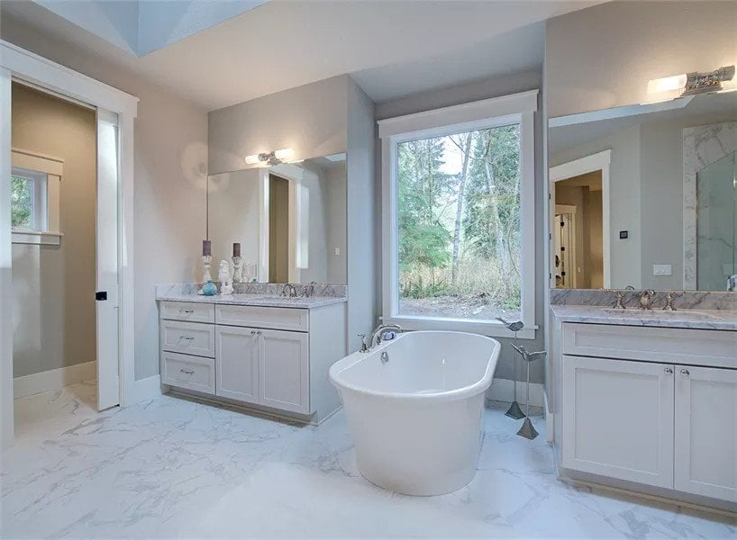 Primary bathroom with a toilet room and a bathtub flanked by his and her vanities.