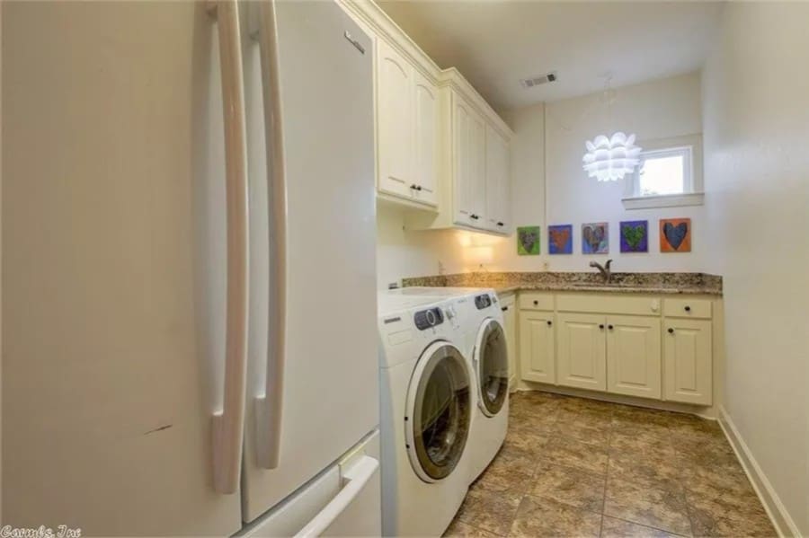 Laundry room with white cabinets, granite counters, and a fridge.