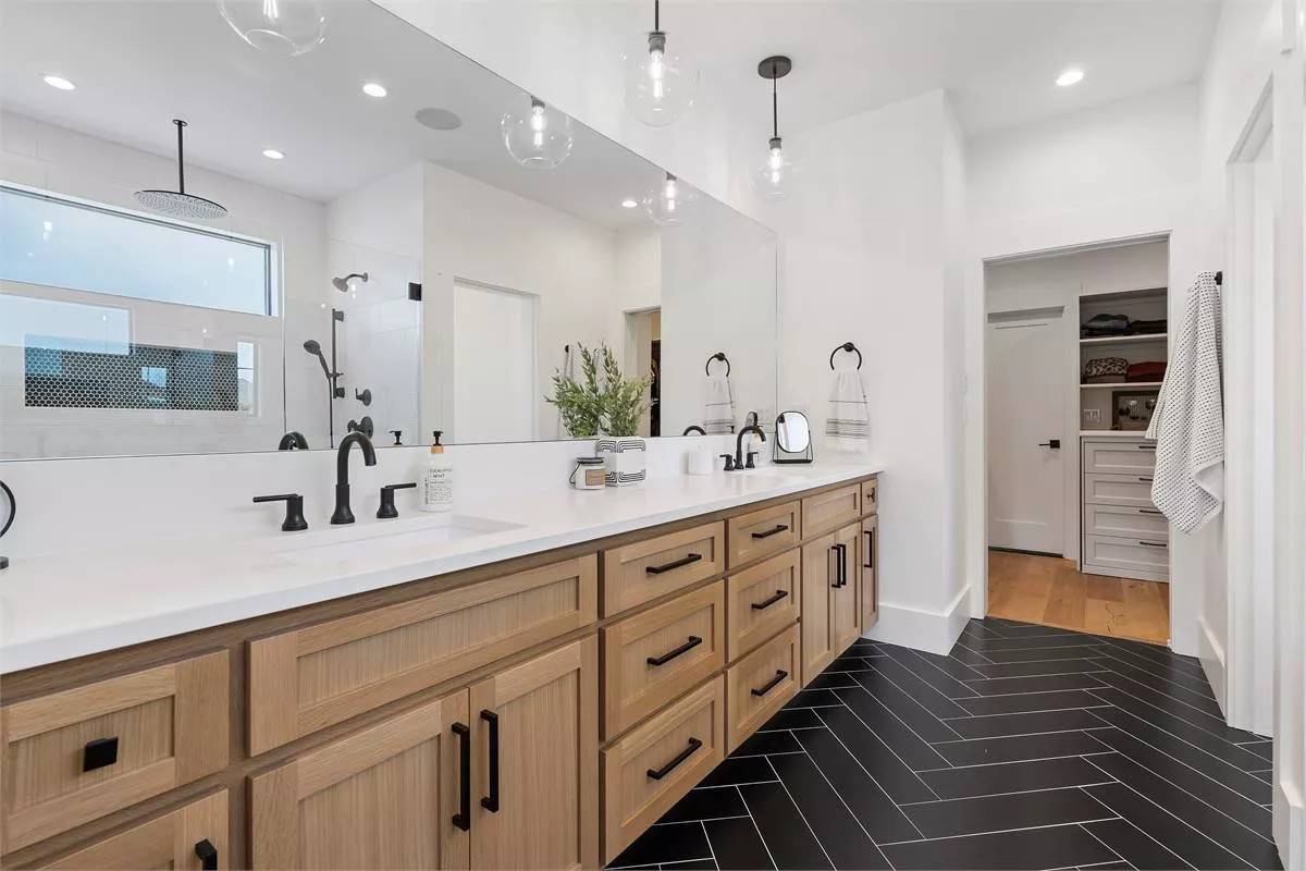 Primary bathroom with a dual sink vanity, herringbone tiled flooring, and a walk-in closet.