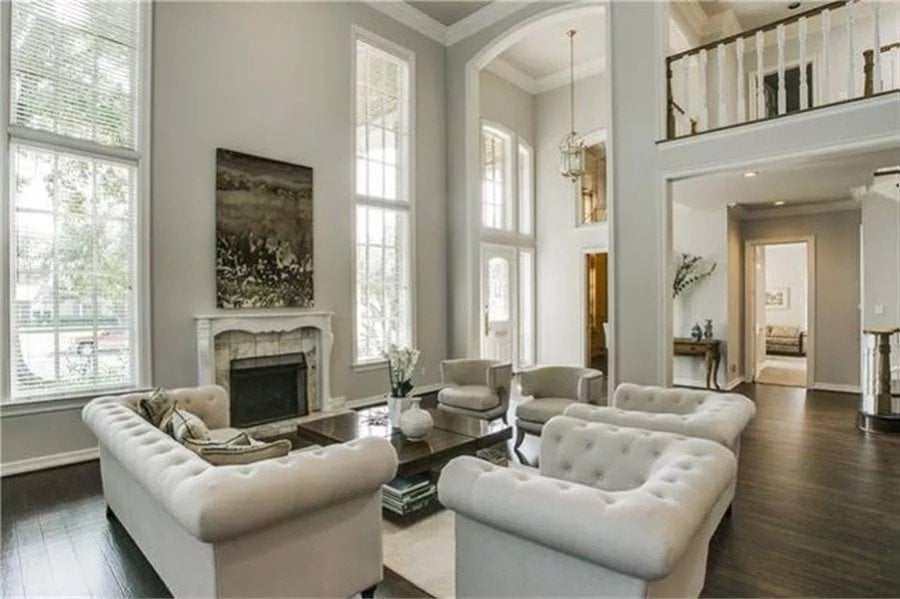 Great room with chesterfield sofas and a fireplace flanked by tall windows.