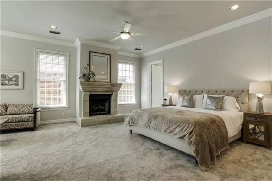 Primary bedroom with a fireplace and a tufted bed over the carpeted flooring.