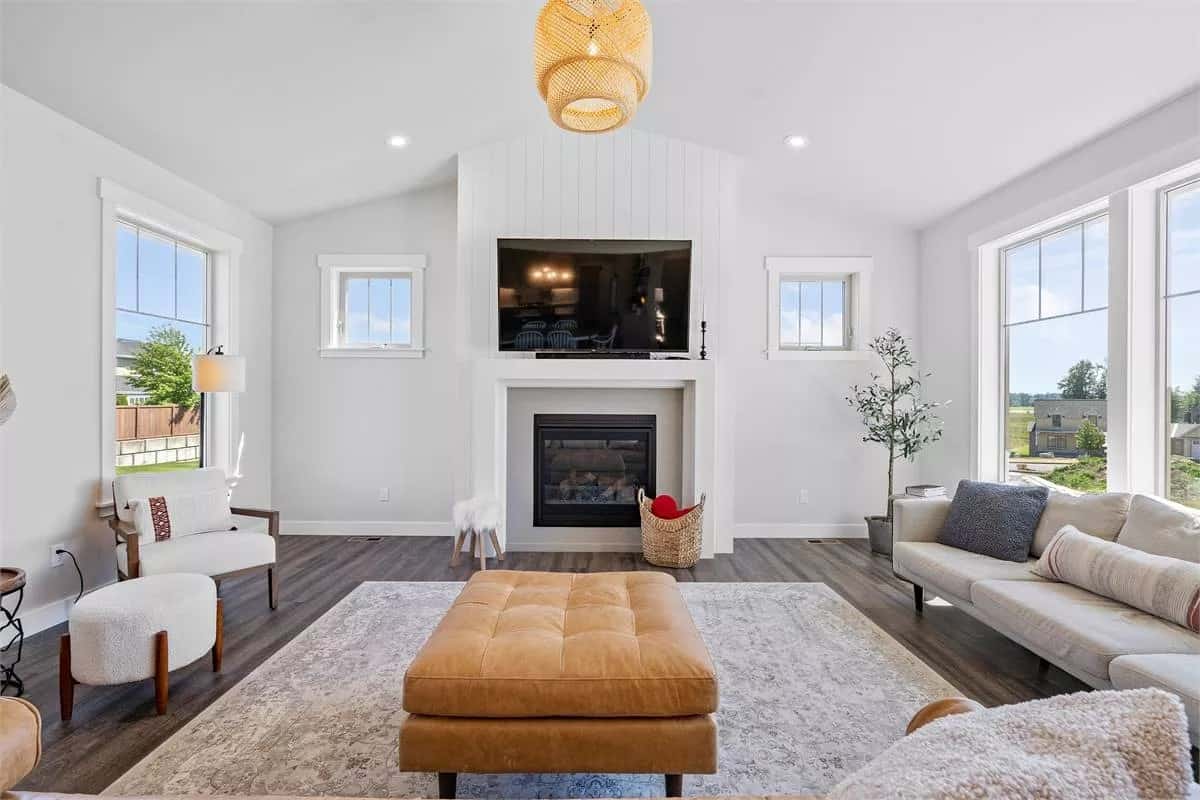 Great room with a sectional sofa, a tufted ottoman, and a fireplace topped with a TV.