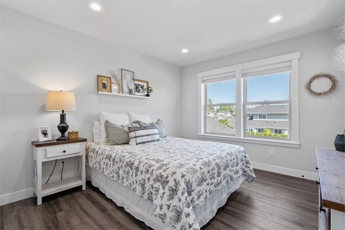Secondary bedroom with white-framed windows and a skirted bed over the hardwood floor.