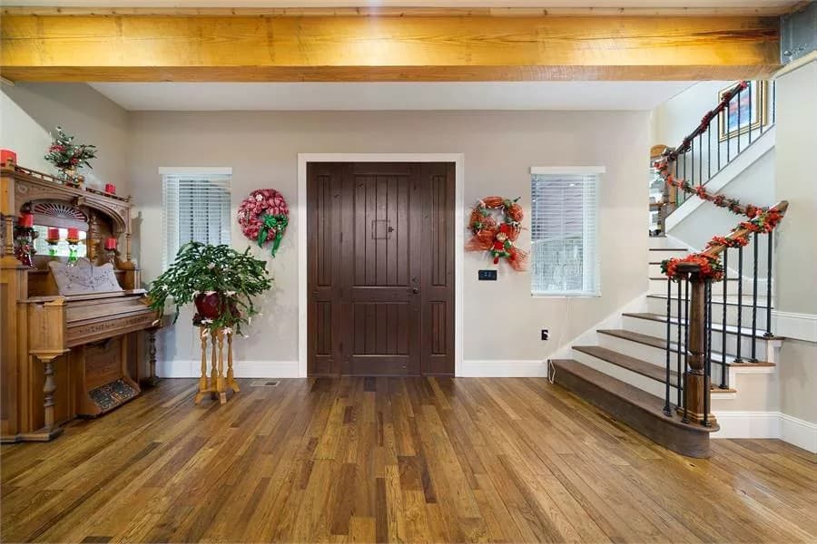 Foyer with a dark wood front door, an upright piano. and a winding staircase.