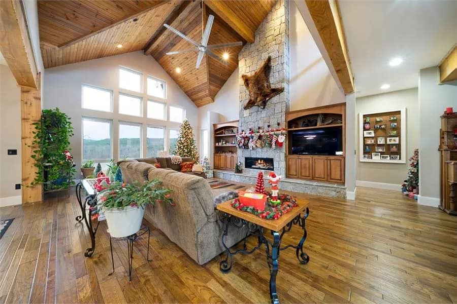 Great room with a velvet sofa, a stone fireplace, and a vaulted ceiling clad in wood planks.