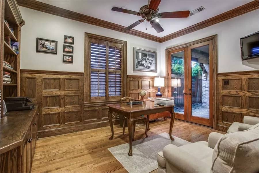 Study with wood-paneled walls, a built-in bookcase, a wooden desk, and a French door that opens onto the outdoor living.