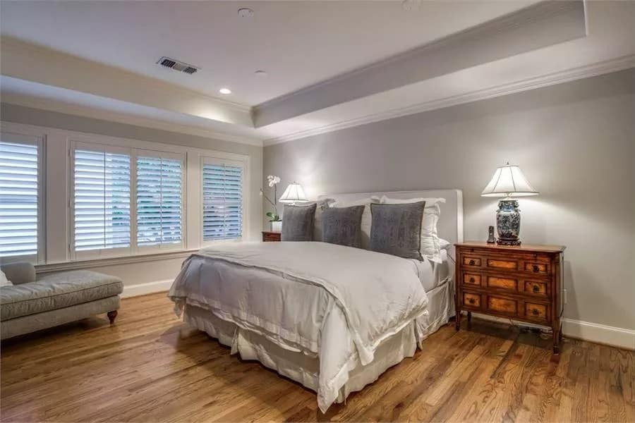 Primary bedroom with a skirted bed and a lounge chair under a tray ceiling.