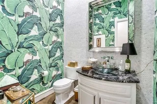 Powder room with a foliage wallpaper and a vessel sink vanity paired with a chrome-framed mirror.