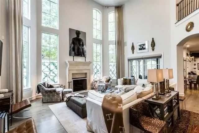 Living room with a tall ceiling, a fireplace, and towering windows bringing natural light in.