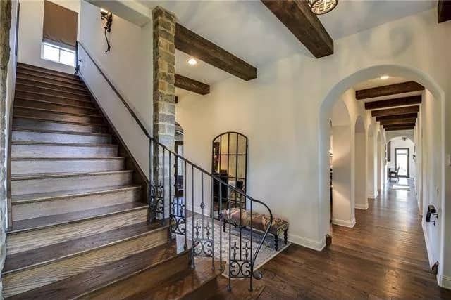 Foyer with an archway, a beamed ceiling, and a staircase framed with wrought iron railings.