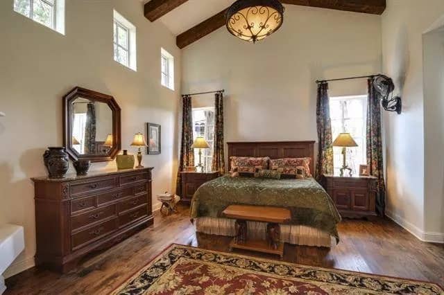 Primary bedroom with wooden furnishings, a vintage area rug, and a vaulted ceiling lined with exposed beams.